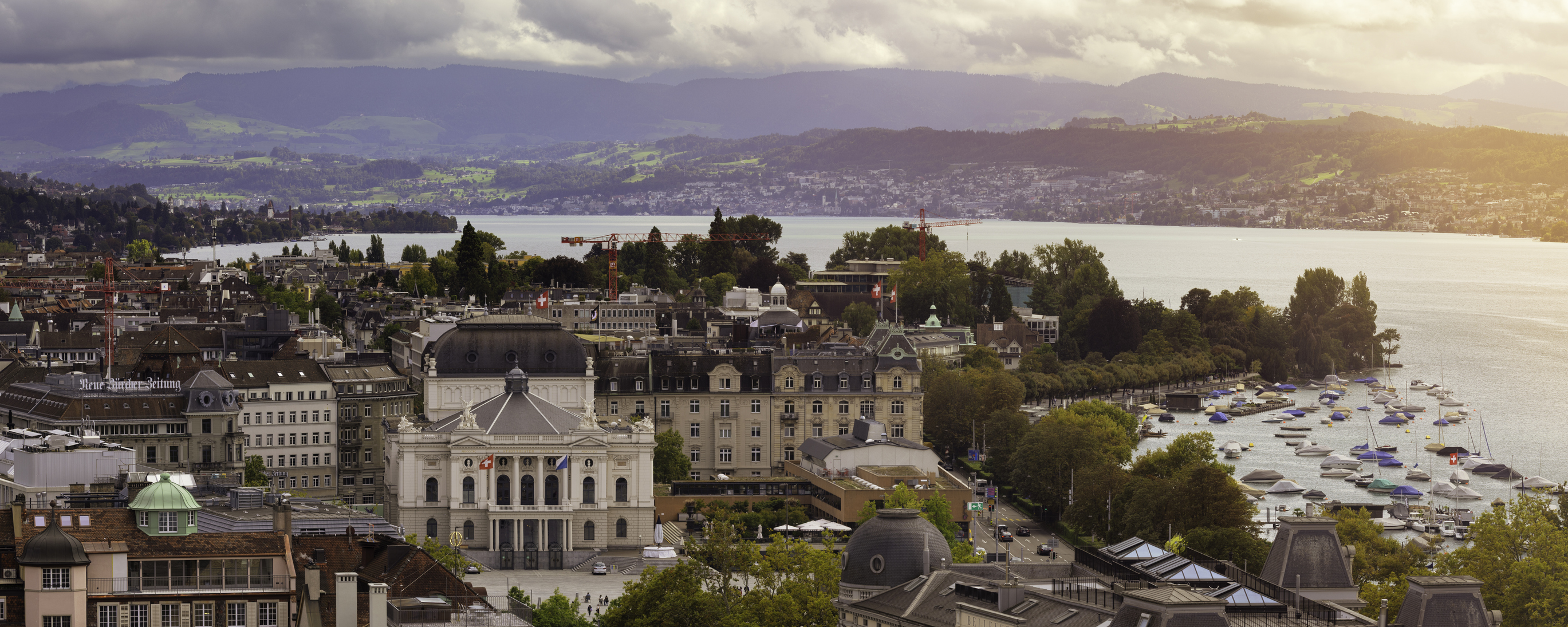 Panoramic view of central Zurich with the Zurich Opera House from 1891 on the left. Behind the city is Lake Zurich and the surrounding mountain landscape.