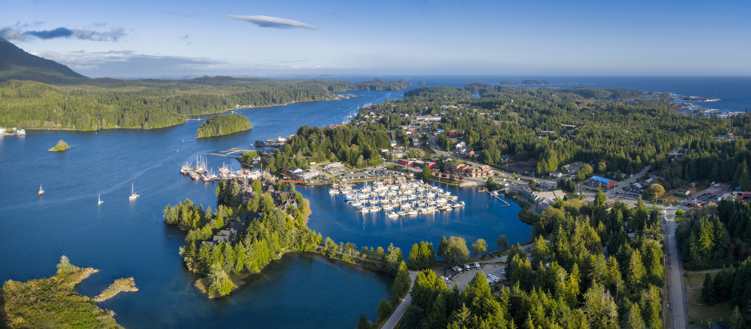 Aerial view of Ucluelet harbor with marina, boats, and surrounding forested coastline along the Pacific Ocean. Scenic coastal town landscape under clear sky in British Columbia. Ucluelet, Vancouver Island, British Columbia, Canada, North America