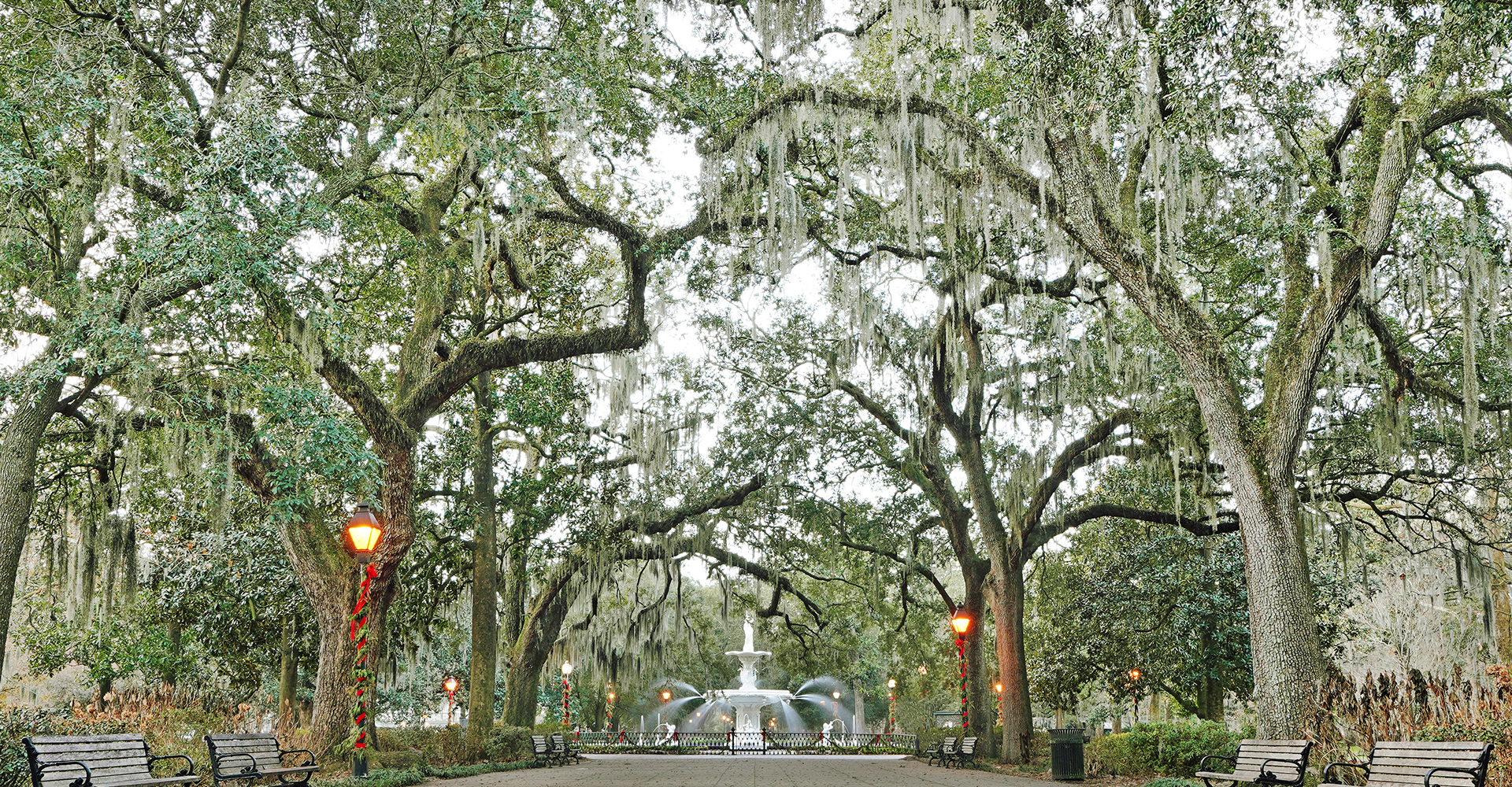 Park path with fountain and large trees.